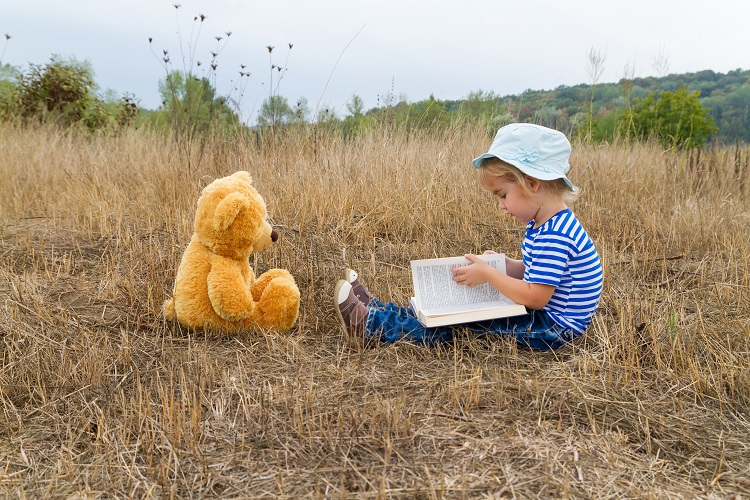 Kid Reading to stuffed animal in a field