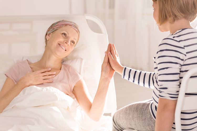 Mother with cancer touching daughter's hand from bed